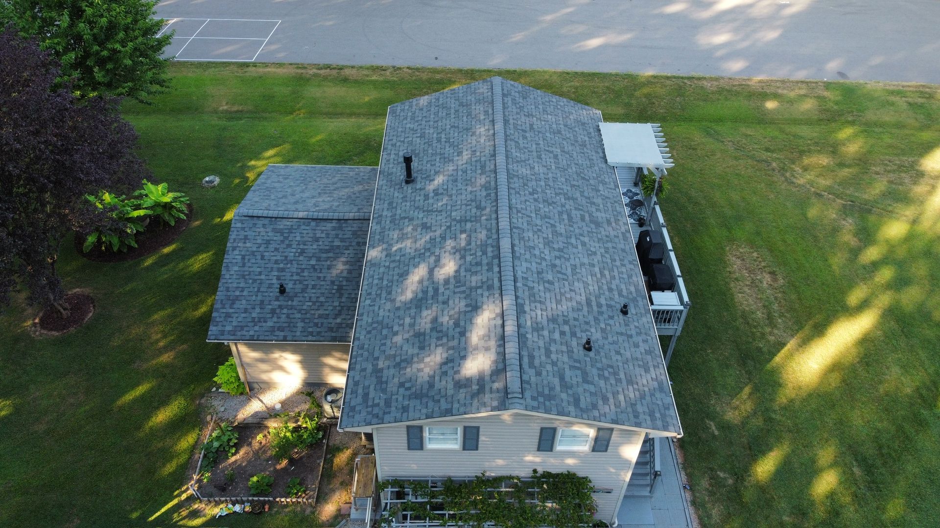 Aerial view of a gray-roofed house with a front porch, surrounded by lawn and trees.