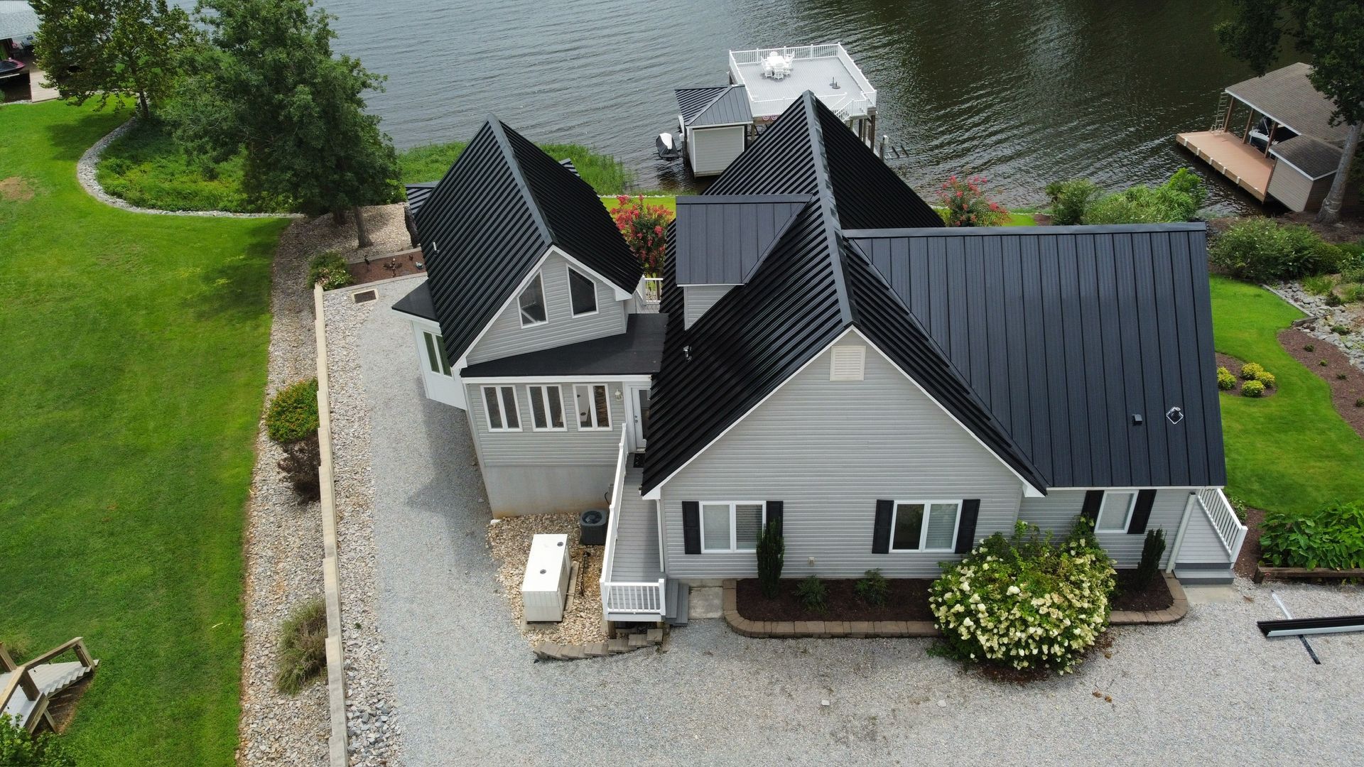 Aerial view of a white lakeside house with a dark roof and gravel driveway beside the water