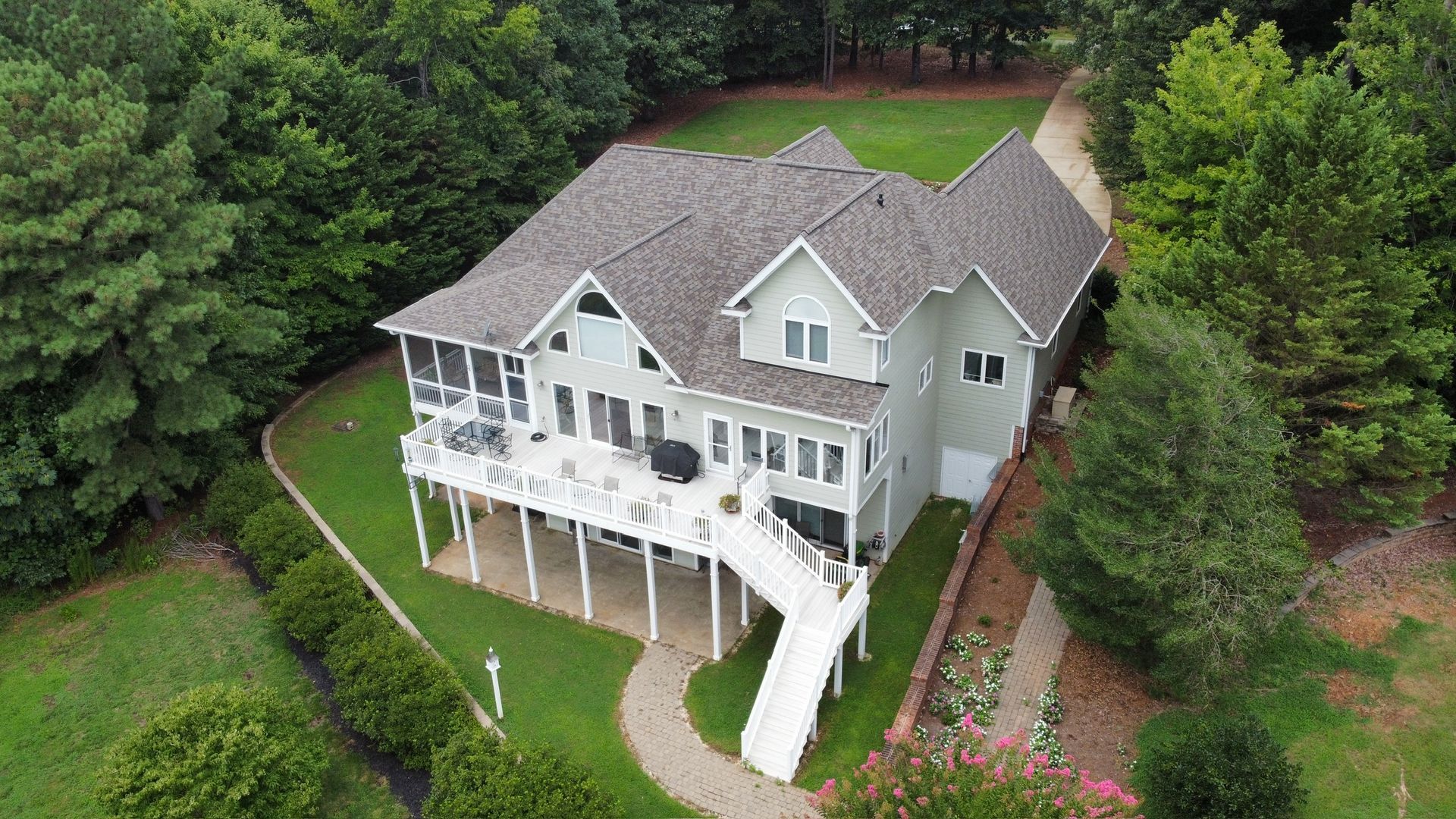 Aerial view of a white house with a wraparound deck, surrounded by dense green trees.