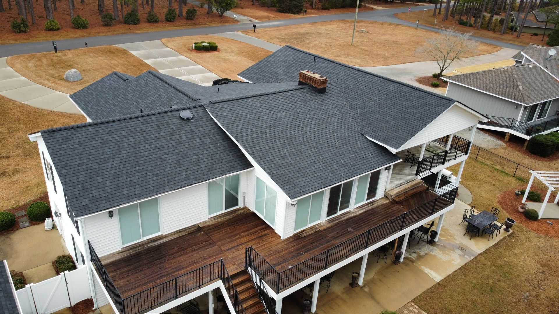 Aerial view of a white house with a dark gray roof and wooden deck in a rural neighborhood.