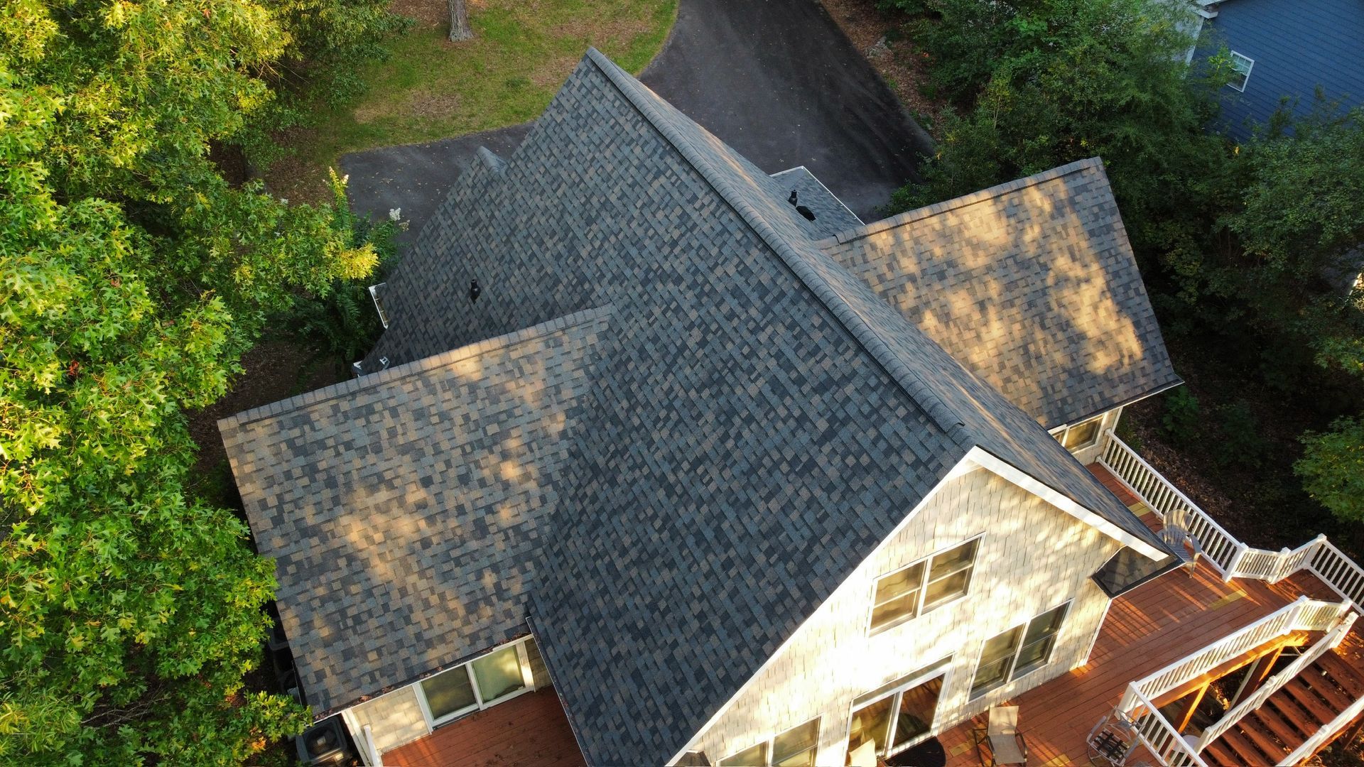 Aerial view of a gray-shingled house roof surrounded by green trees and a brick patio