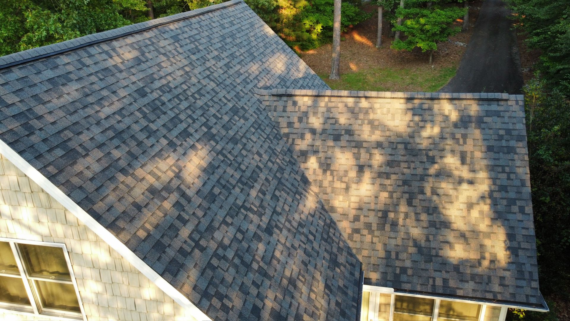 Aerial view of a house roof with gray shingles and sunlight casting tree shadows.