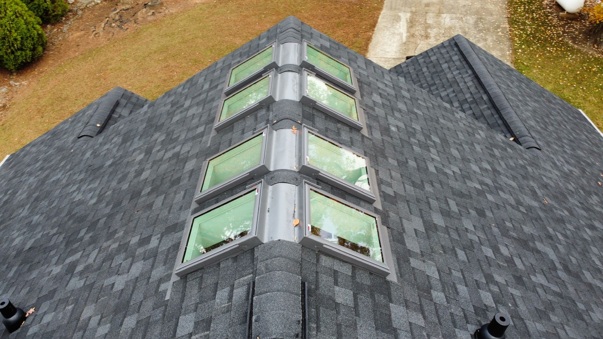 Steep gray shingle roof with central dormer windows and green trim on a house