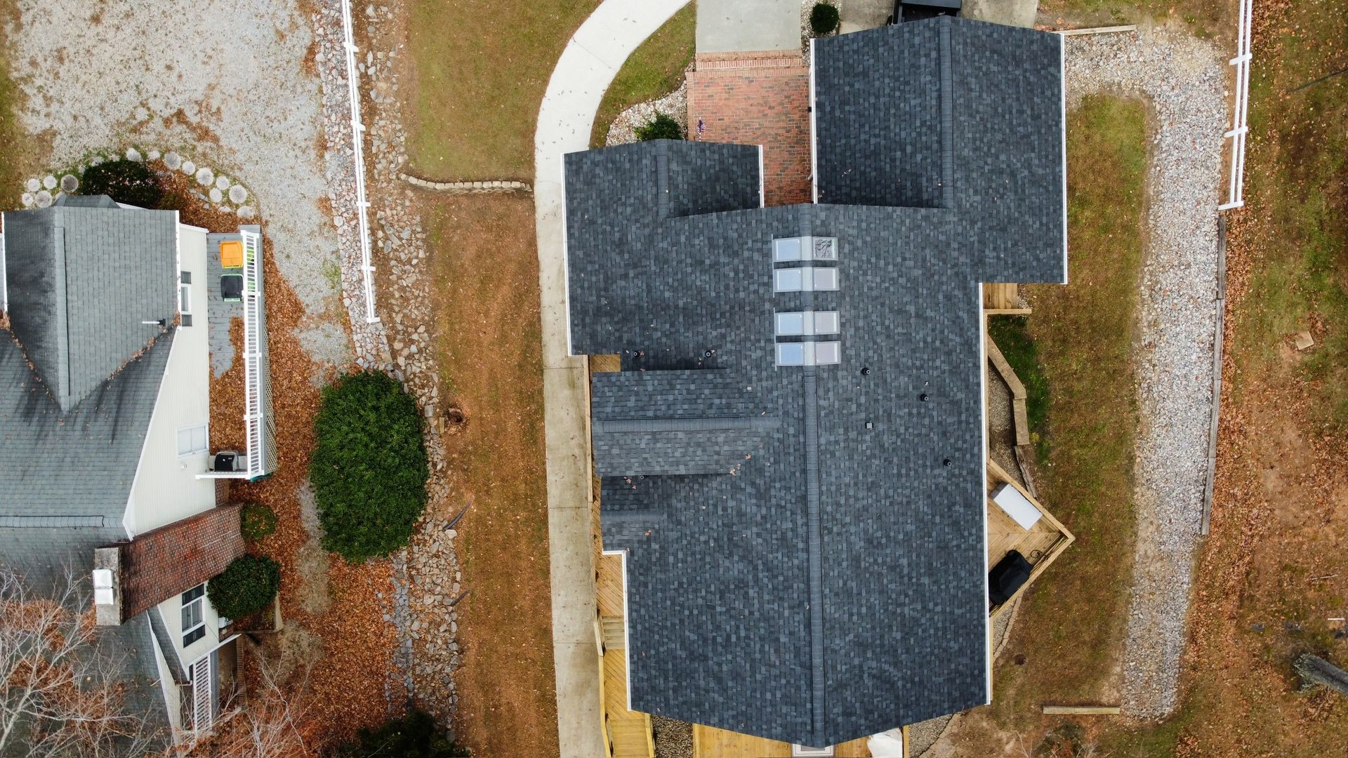 Aerial view of a dark gray roofed house with a driveway, yard, and neighboring homes.