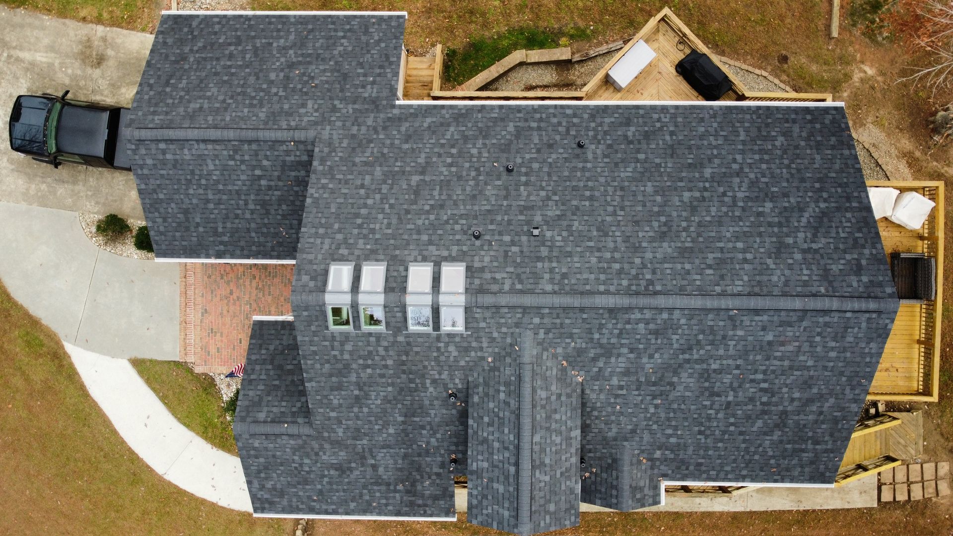 Aerial view of a house with a dark gray roof, skylights, and a driveway with a parked truck.