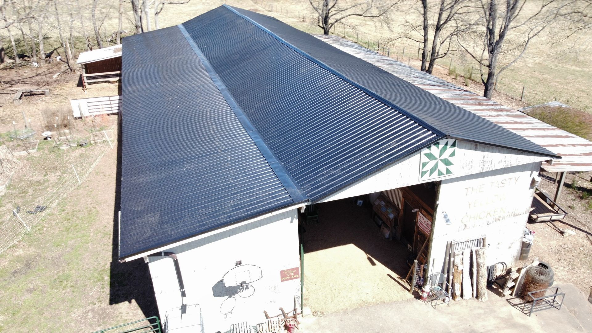 Aerial view of a white barn with a dark metal roof in a rural setting.