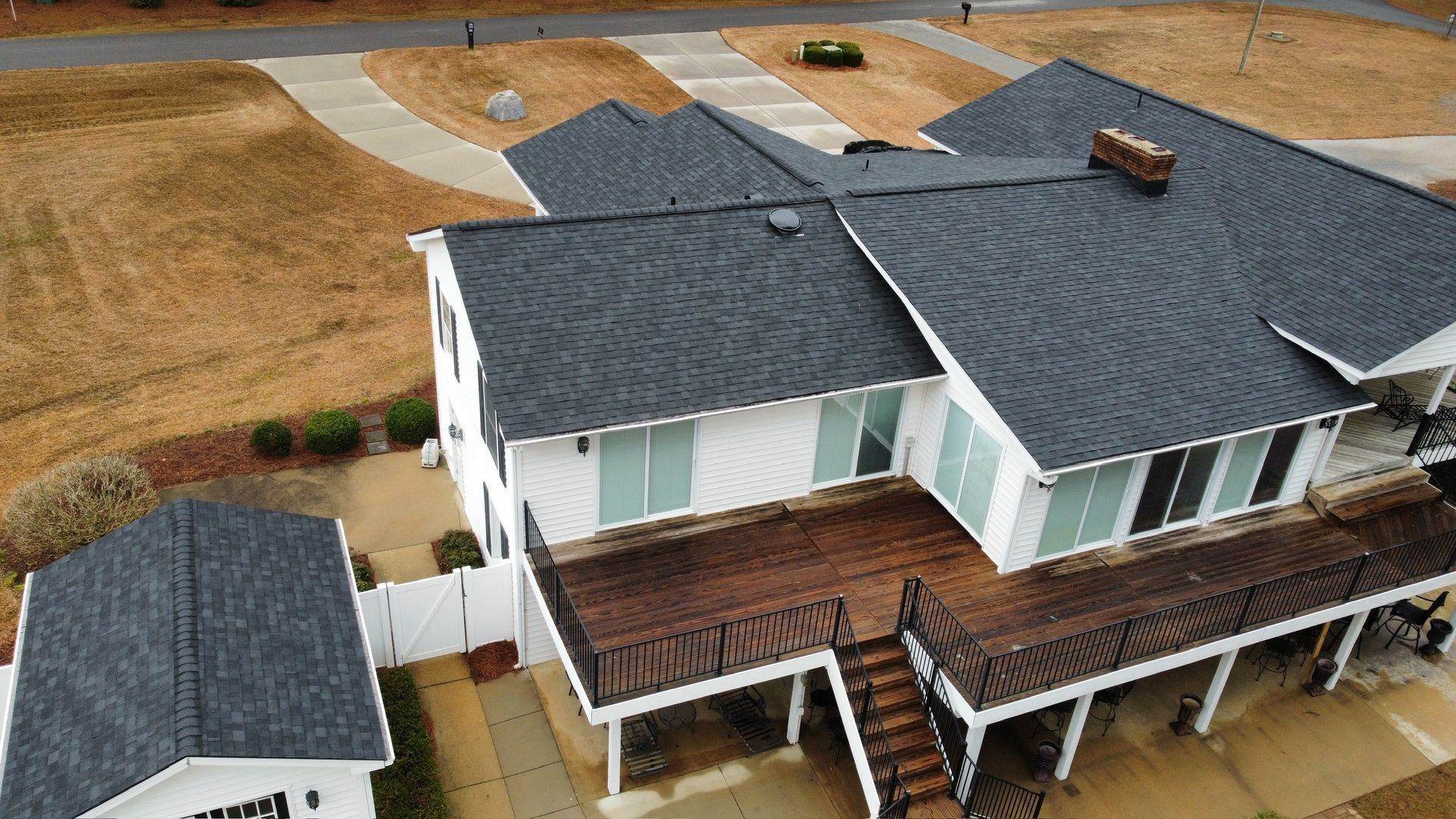 Aerial view of a white house with a dark roof and wooden deck in a suburban neighborhood.