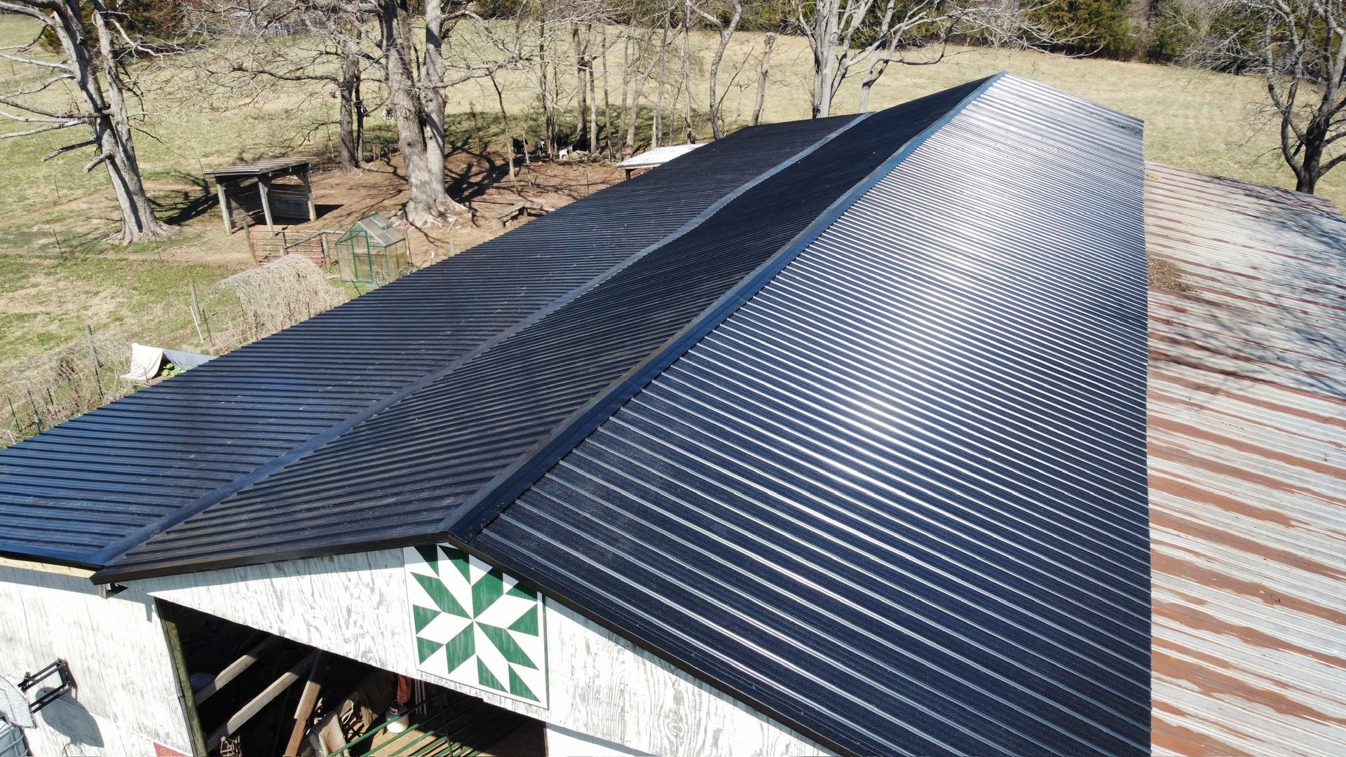 Roof with a newly installed black metal covering on a rural building, viewed from above.