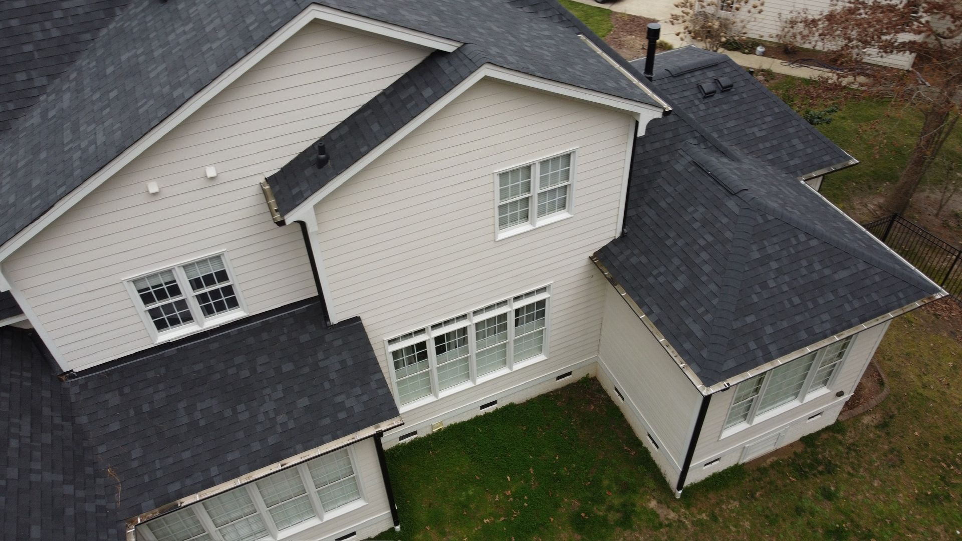 Aerial view of a gray suburban house with white trim and dark shingled roofs.