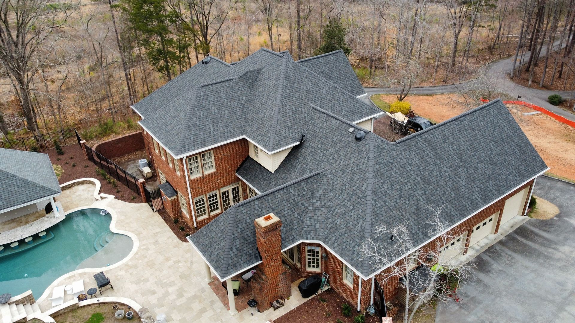 Aerial view of a large brick house with a gray roof and backyard pool surrounded by trees.