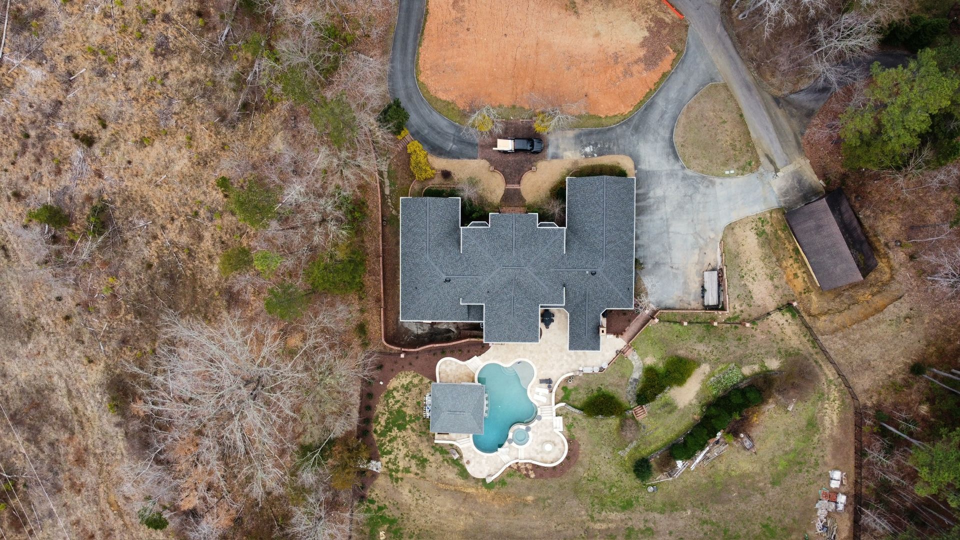 Aerial view of a house with a blue backyard pool, driveway, and surrounding trees.