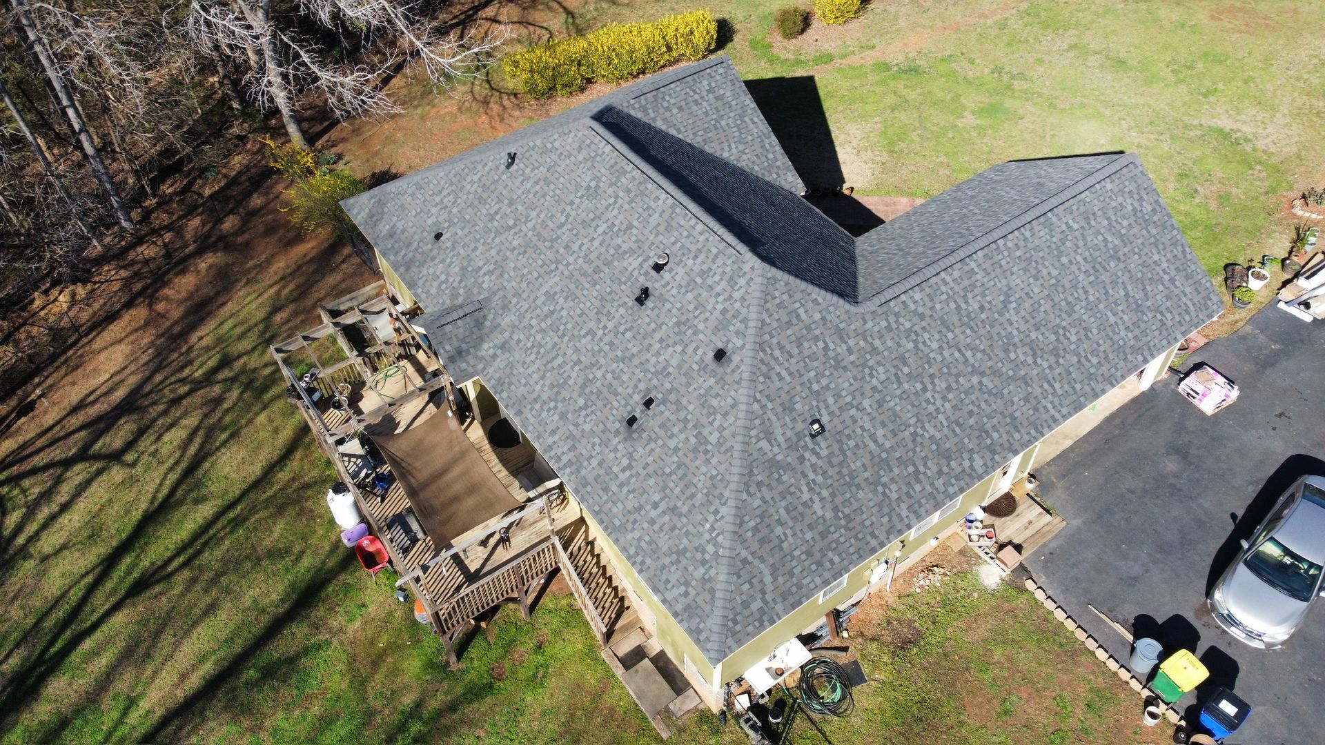 Aerial view of a house with a gray roof, backyard deck, and a parked car beside the driveway.