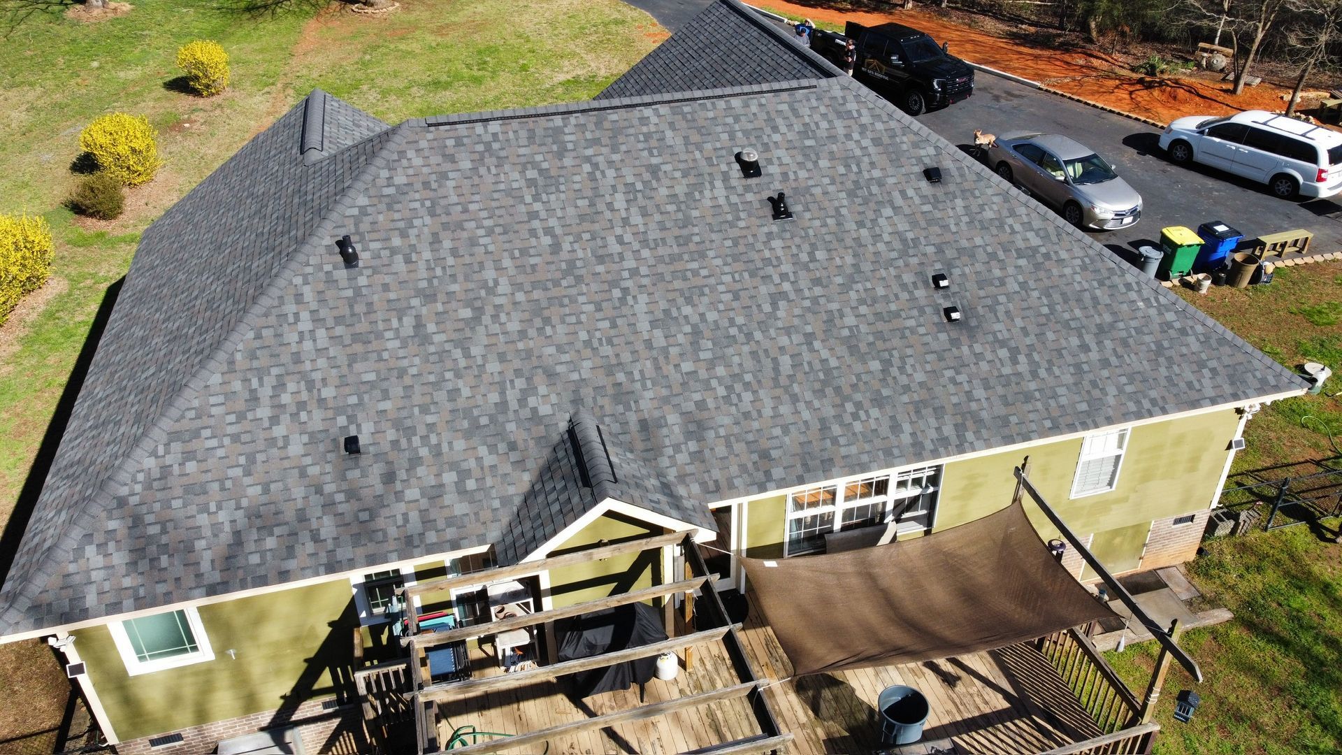 Aerial view of a house with a gray roof, backyard deck, and parked cars nearby.