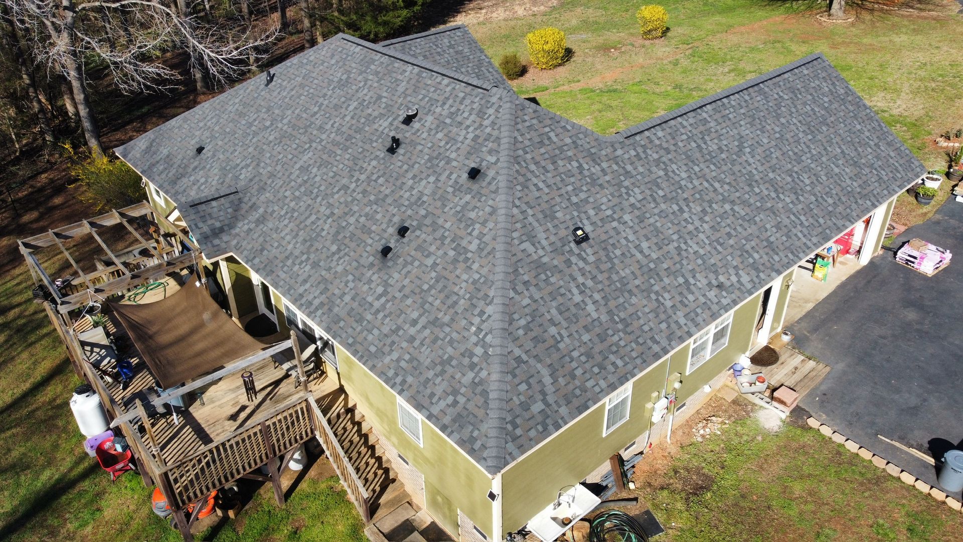 Aerial view of a house with a gray roof and beige siding, surrounded by yard and driveway.