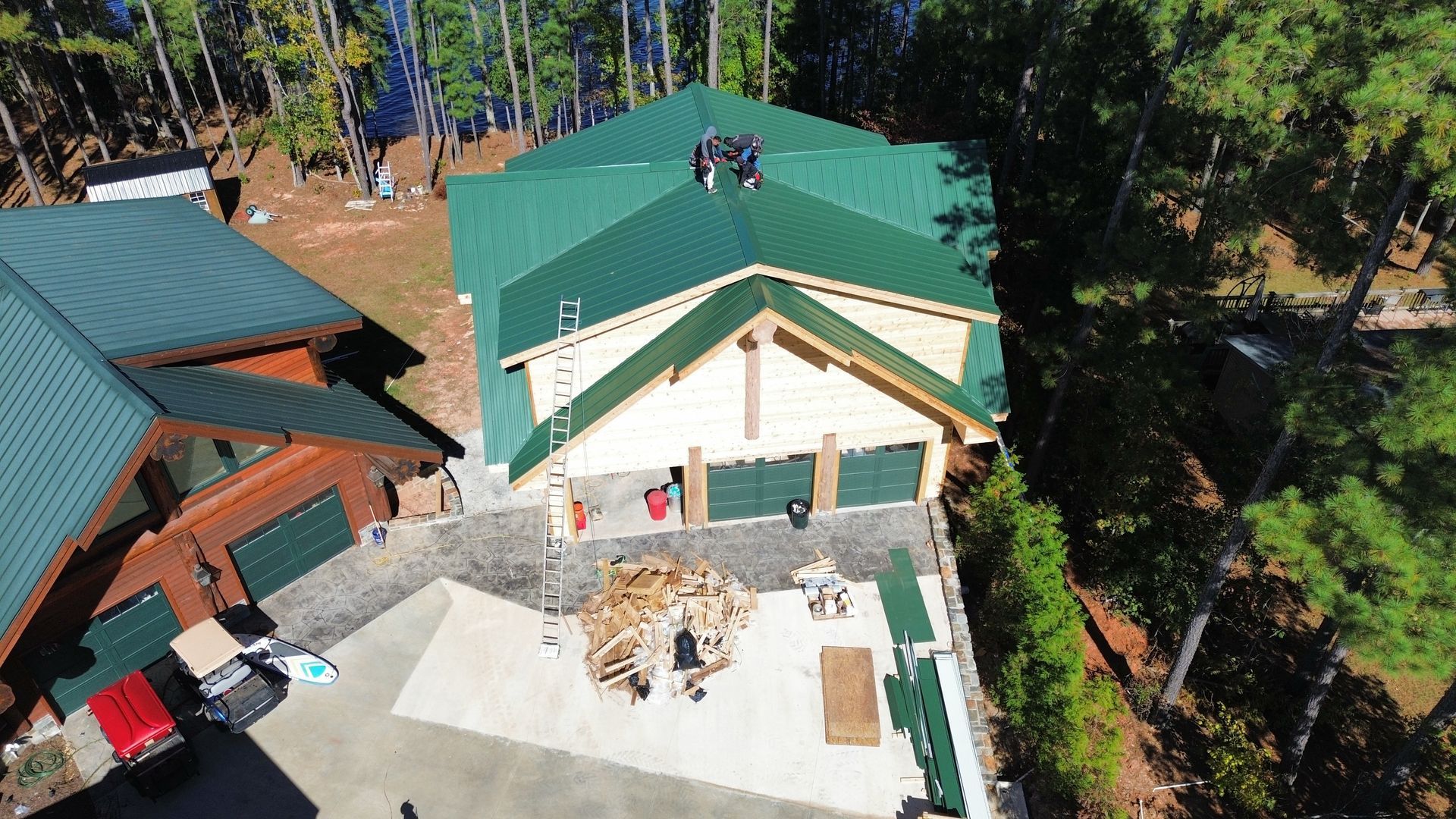 Aerial view of a green-roofed house with a sunlit concrete courtyard and surrounding trees.