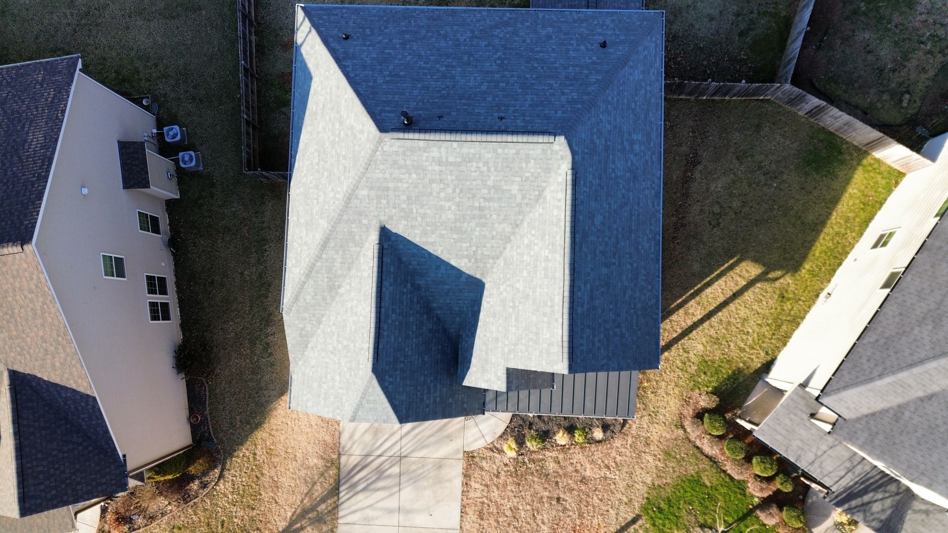 Aerial view of a house with a gray roof, driveway, and neighboring homes on both sides.