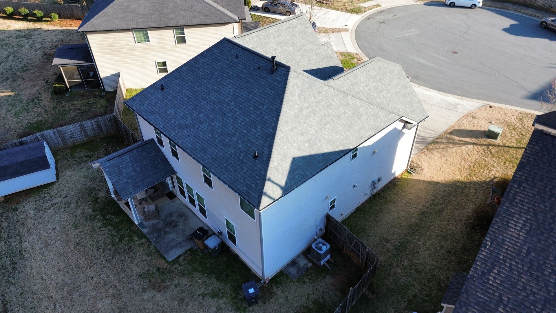 Aerial view of a white house with a dark roof and backyard in a suburban neighborhood