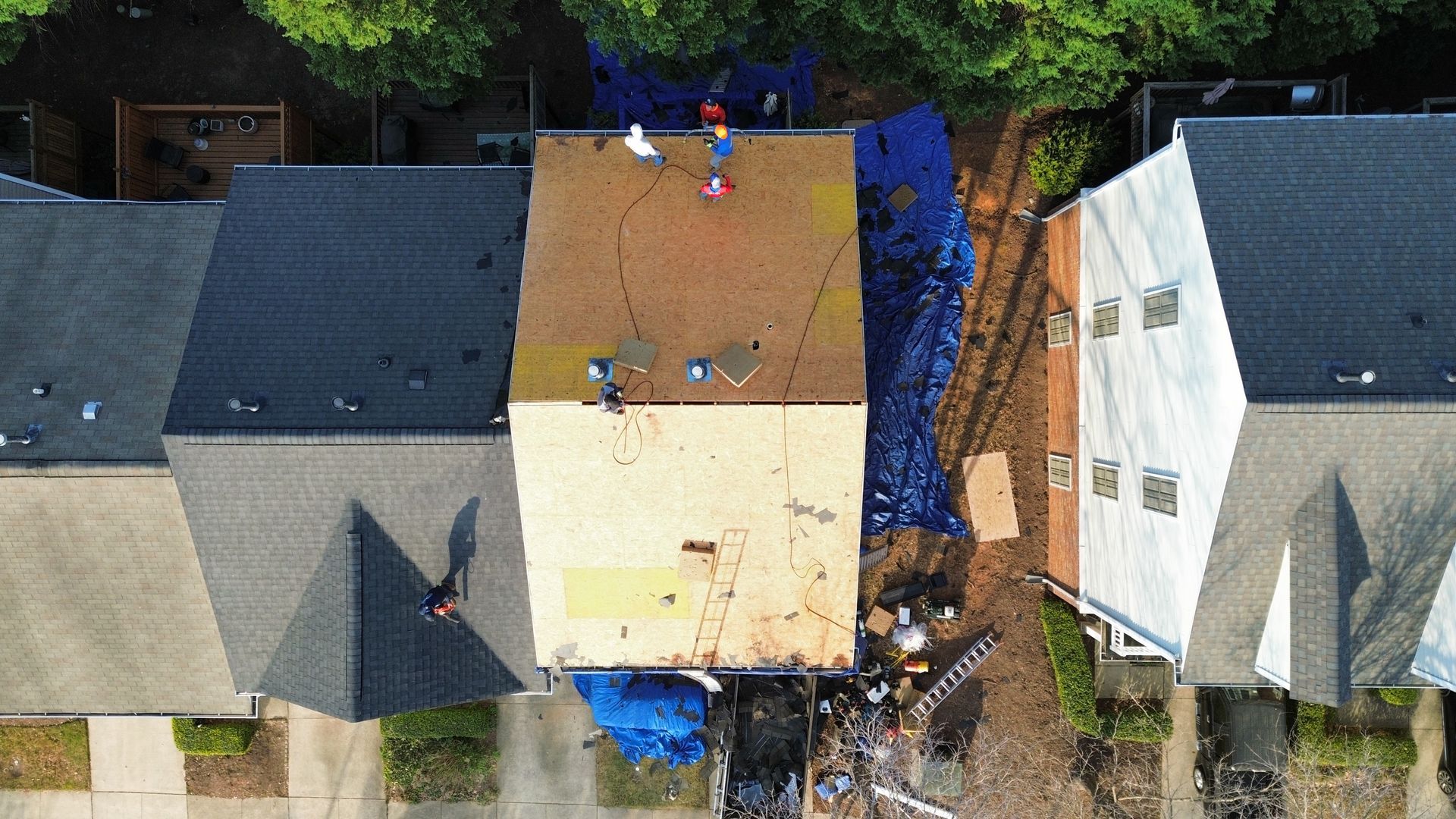 Aerial view of three adjacent houses, with workers and blue tarps on the central roof under repair