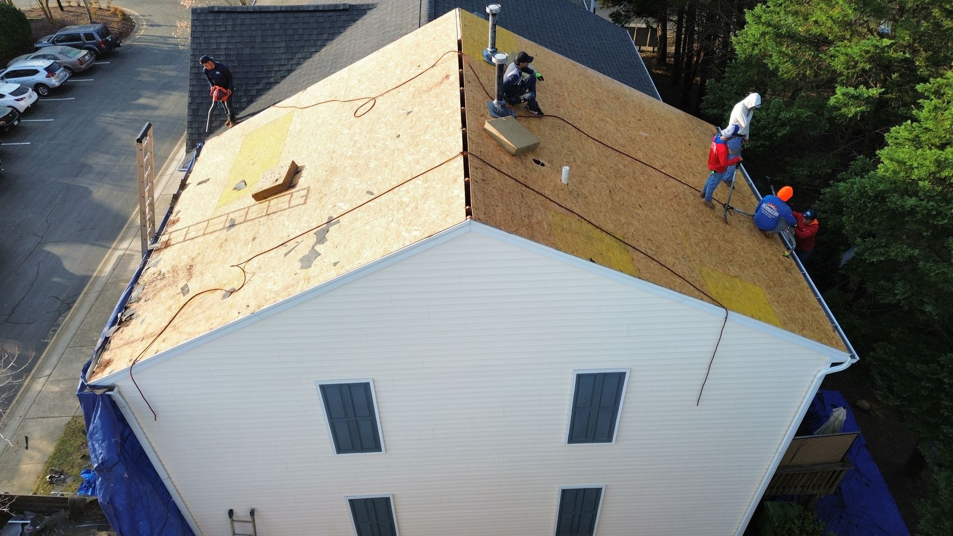 Workers repairing a residential roof with plywood sheathing and tarps, viewed from above