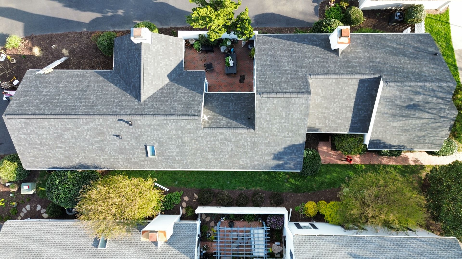 Aerial view of a gray-roofed suburban house with chimney, skylights, and a small patio below