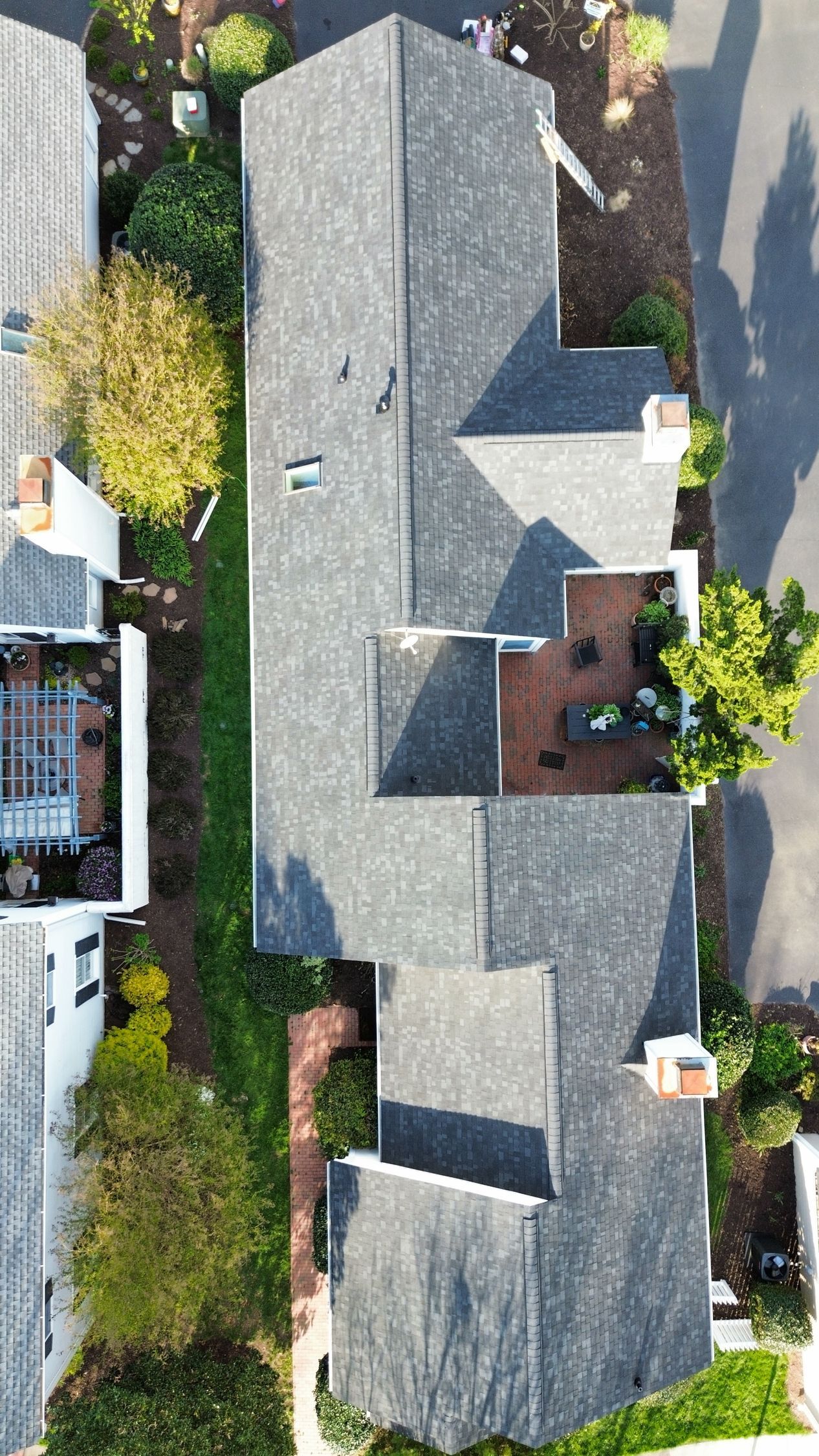 Aerial view of a house with a gray roof, surrounded by trees and neighboring homes.
