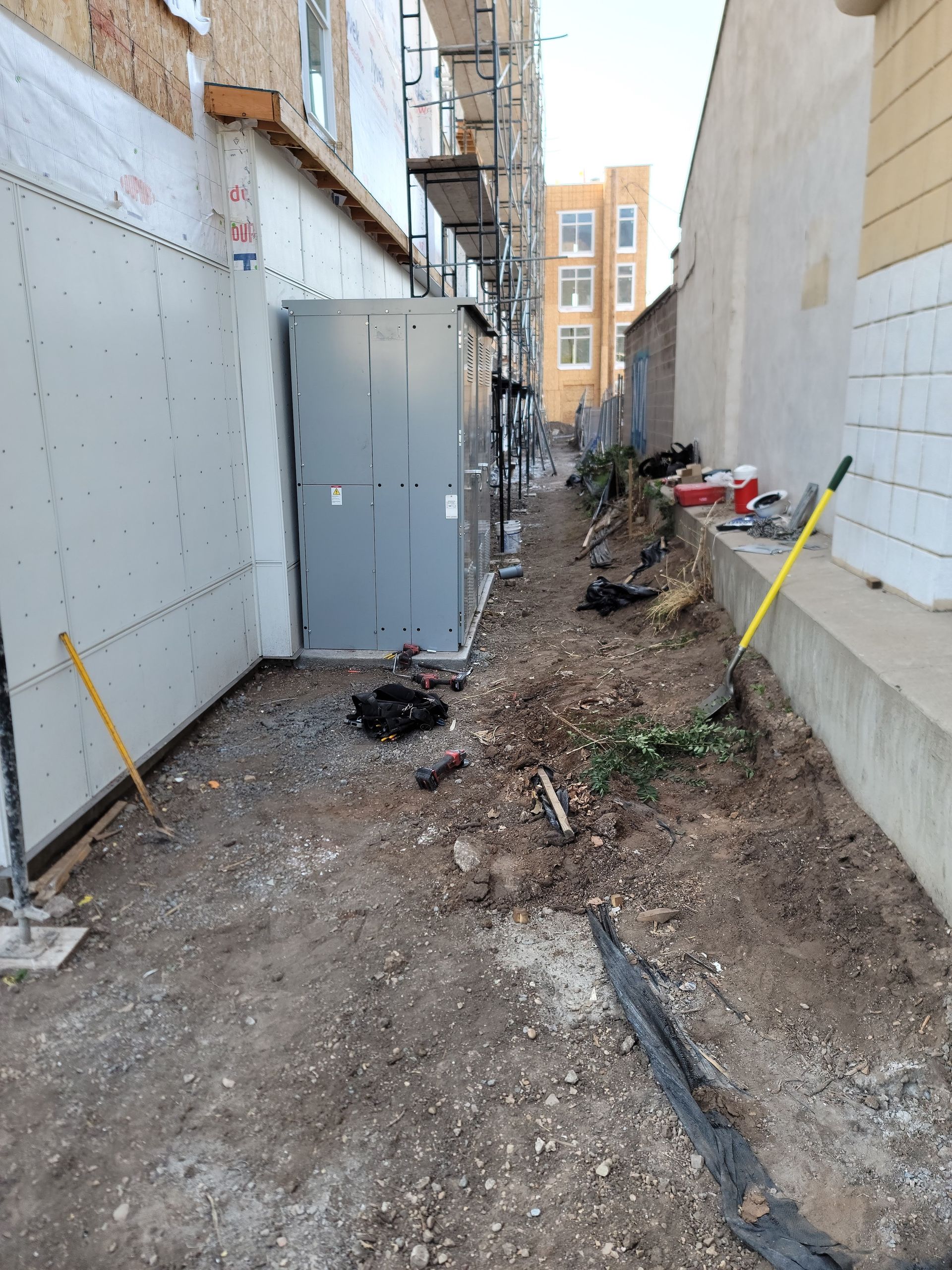 A narrow alleyway between two buildings with shovels in the dirt