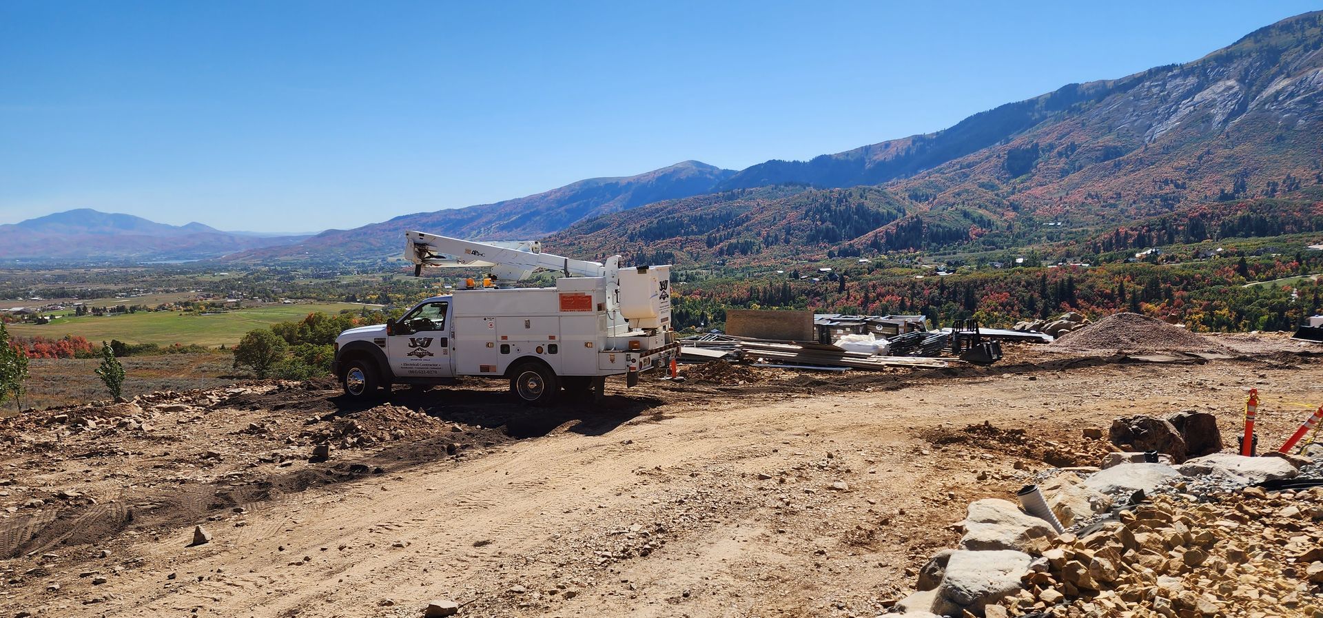 A white truck is parked in a dirt field with mountains in the background.