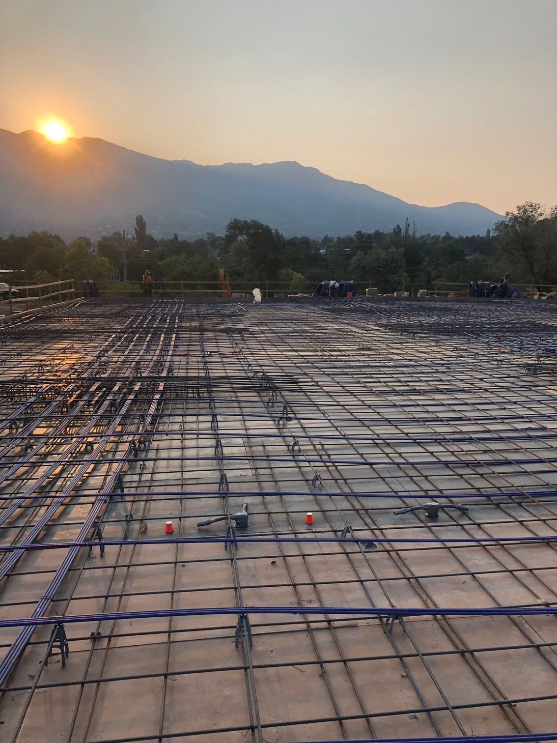 The sun is setting over a construction site with mountains in the background.