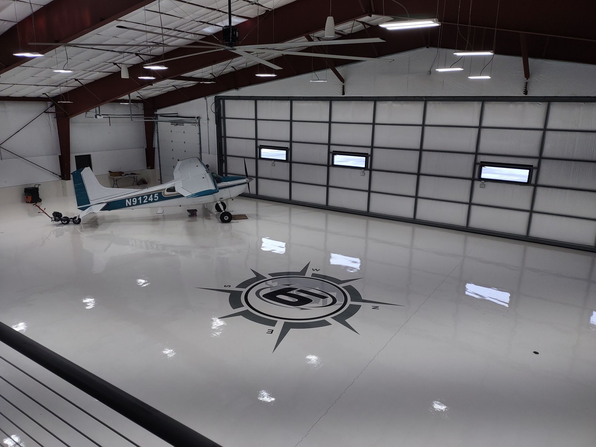 A small plane is parked in a hangar with a compass on the floor.