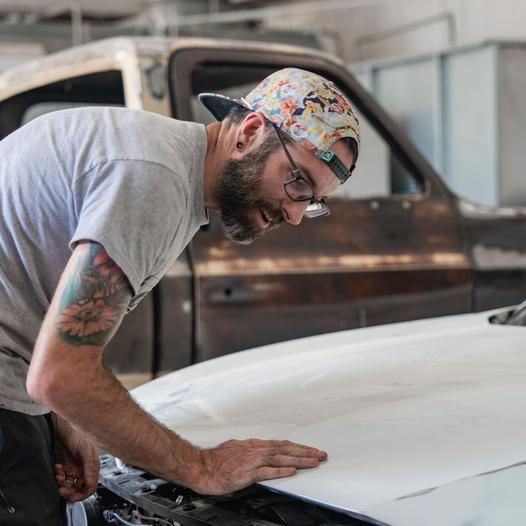 A man is repairing the hood of a car in an automotive repair shop