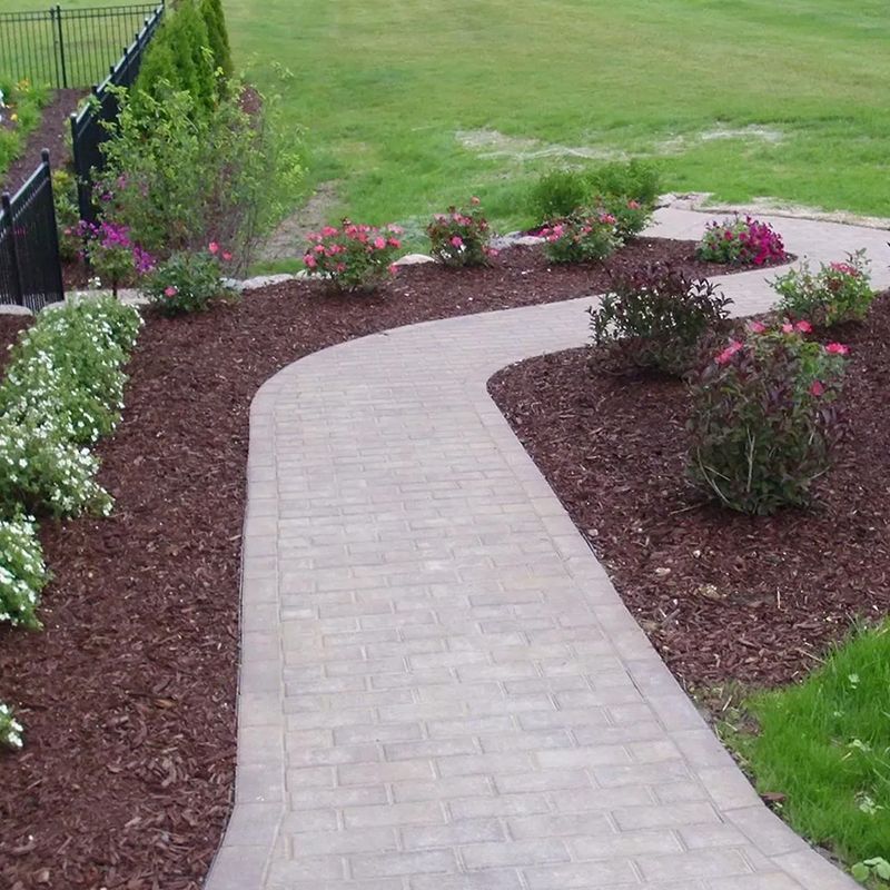 A brick walkway is surrounded by flowers and mulch