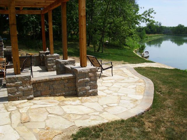 a patio with a pergola and a fireplace overlooking a lake