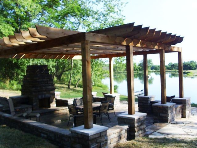 A wooden pergola over a patio with a fireplace