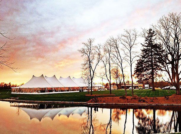 a large white tent is sitting next to a lake at sunset