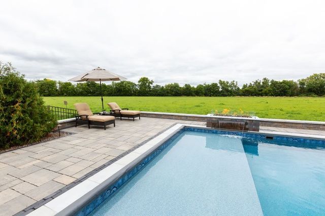 a large swimming pool surrounded by chairs and umbrellas with a field in the background .
