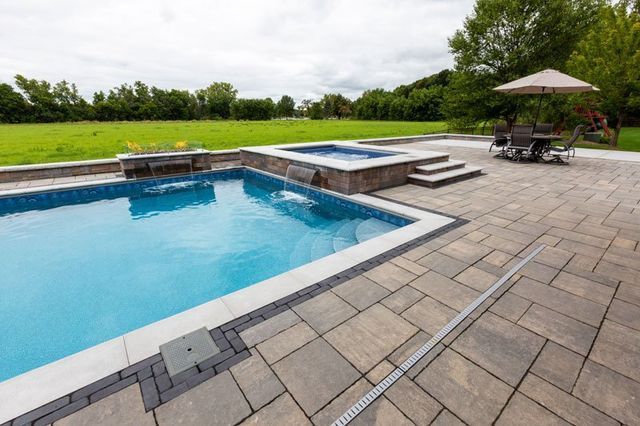 a large swimming pool is surrounded by a patio and a table and chairs .