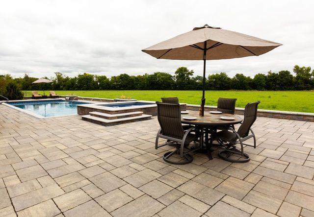 a patio with a table and chairs and an umbrella next to a pool .