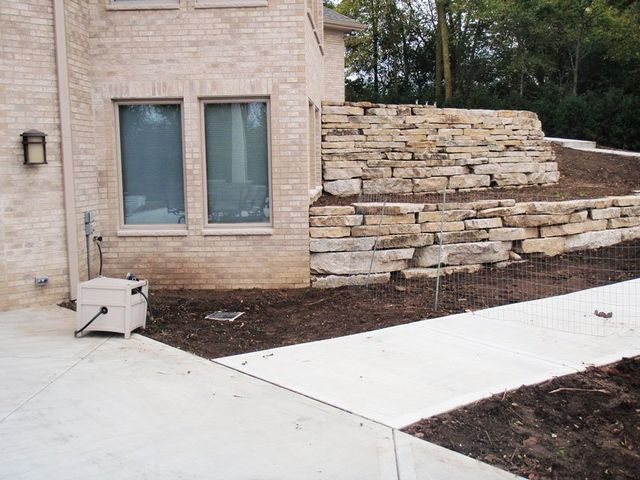 a brick house with a stone wall and a sidewalk in front of it .