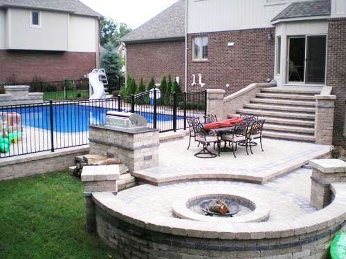 a patio with a fire pit and a pool in the background