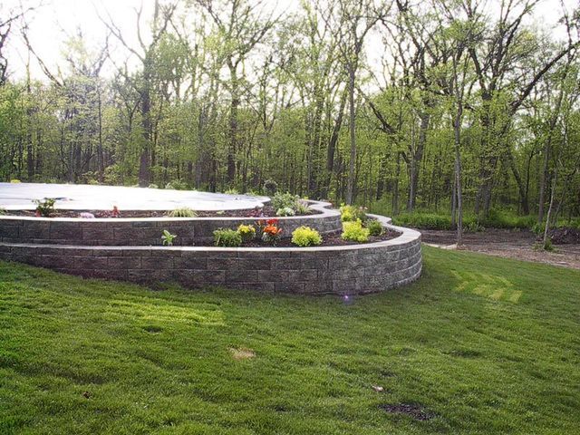 a lush green field with a brick wall and trees in the background