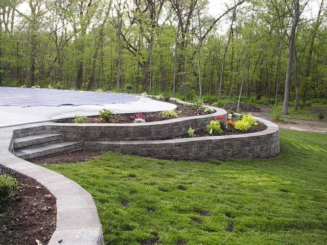 a swimming pool is surrounded by a stone wall and a lush green lawn .