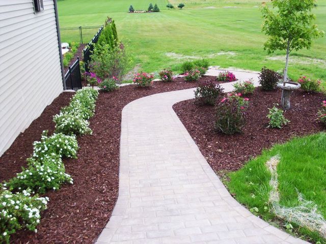 a walkway leading to a house surrounded by flowers and mulch