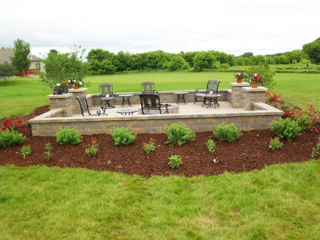 a patio with tables and chairs in the middle of a lush green field .