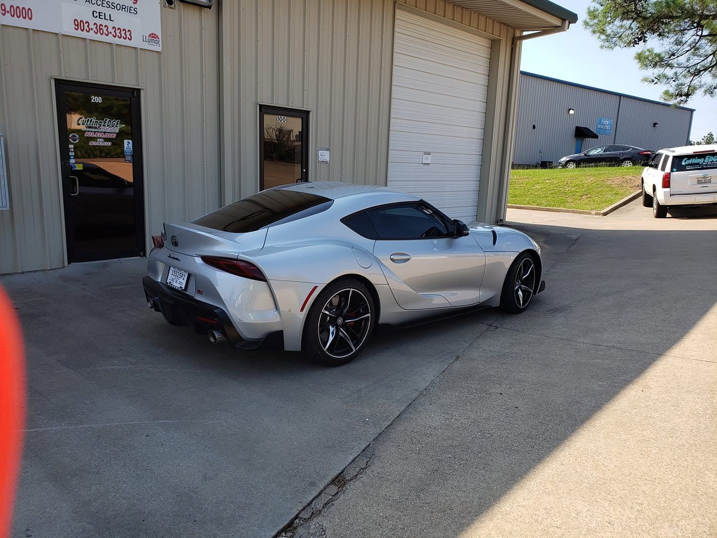 Silver sports car parked beside a warehouse garage in bright daylight