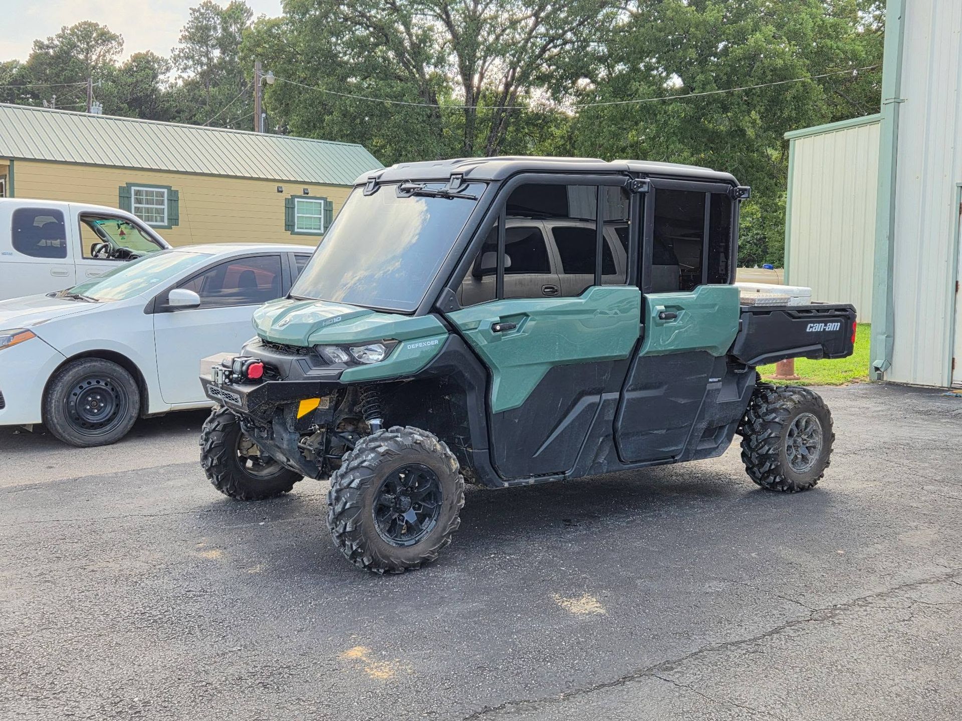 Black and green off-road side-by-side utility vehicle parked on gravel near buildings and cars