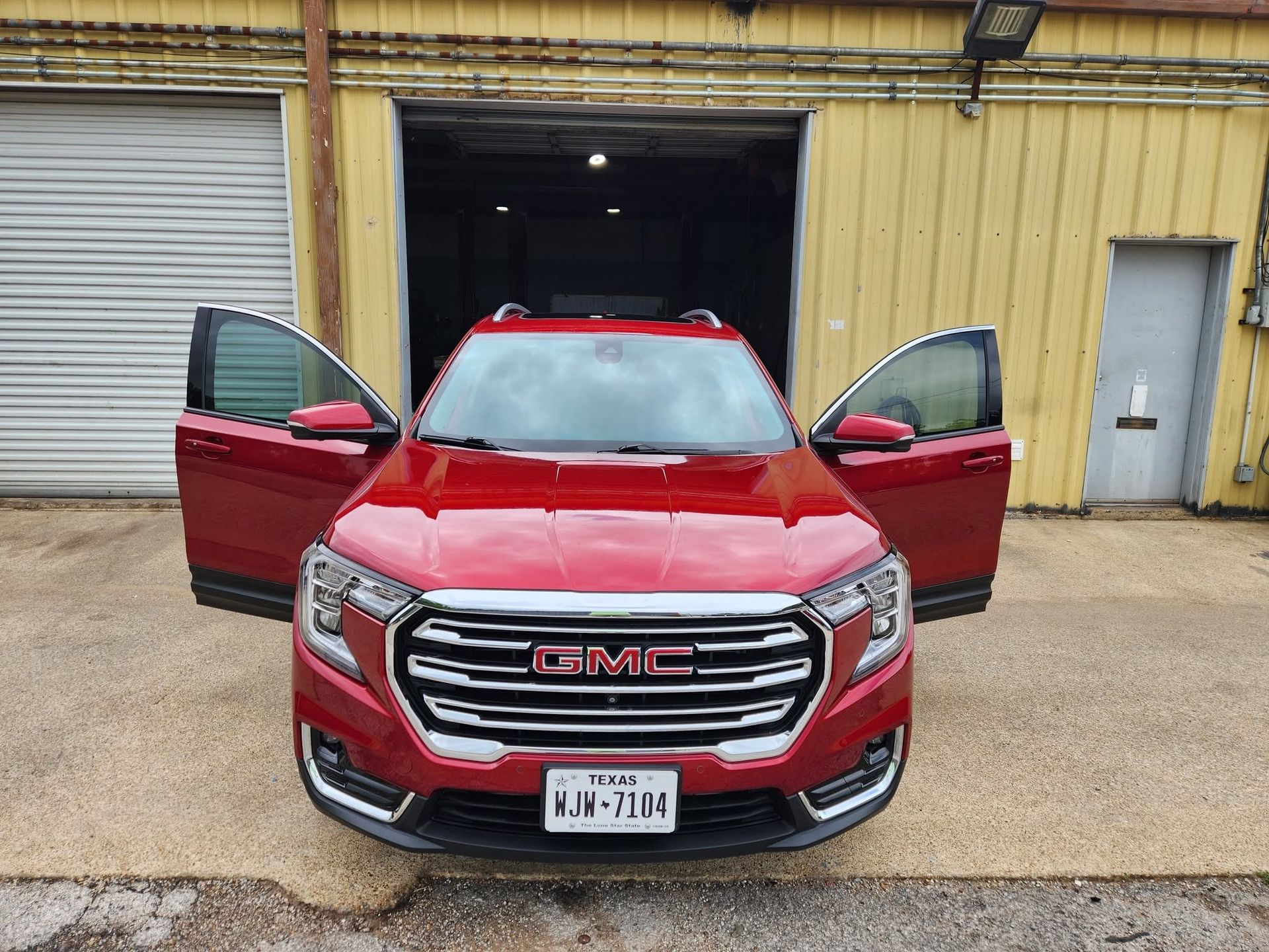 Red GMC SUV with both front doors open in front of a warehouse