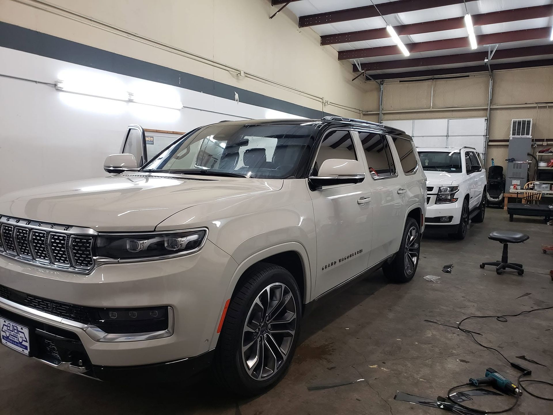 Two beige SUVs in an auto shop, one in front under repair with tools on the floor.
