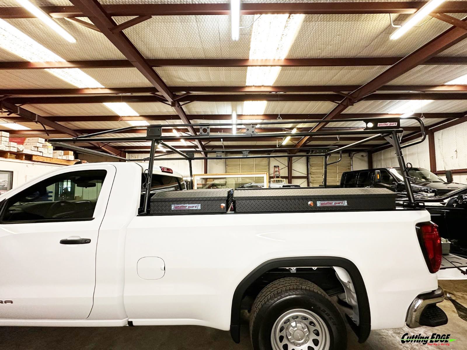 White pickup truck with a black utility bed parked inside an auto shop garage