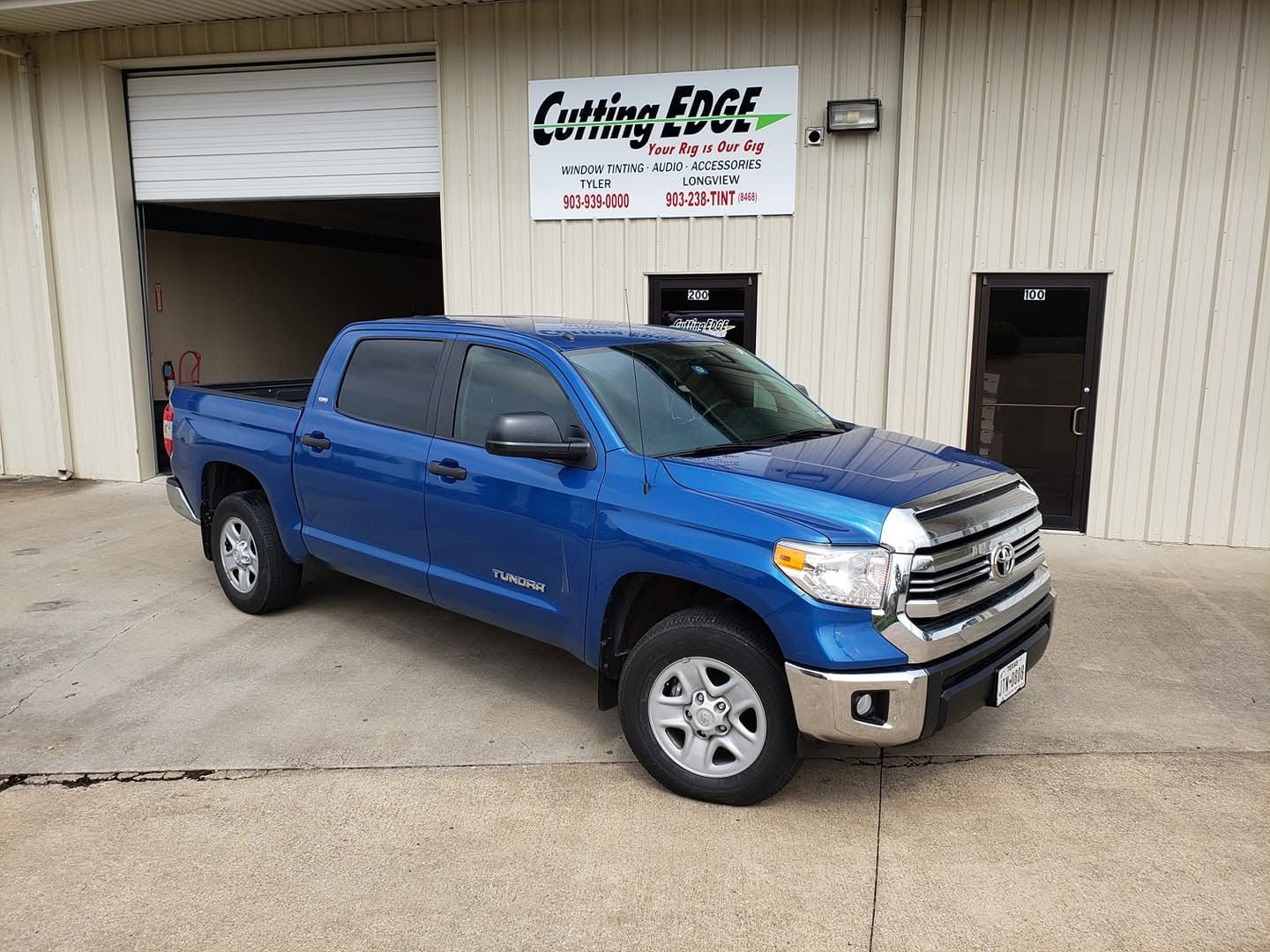Blue pickup truck parked outside a shop with a white sign above the garage door.