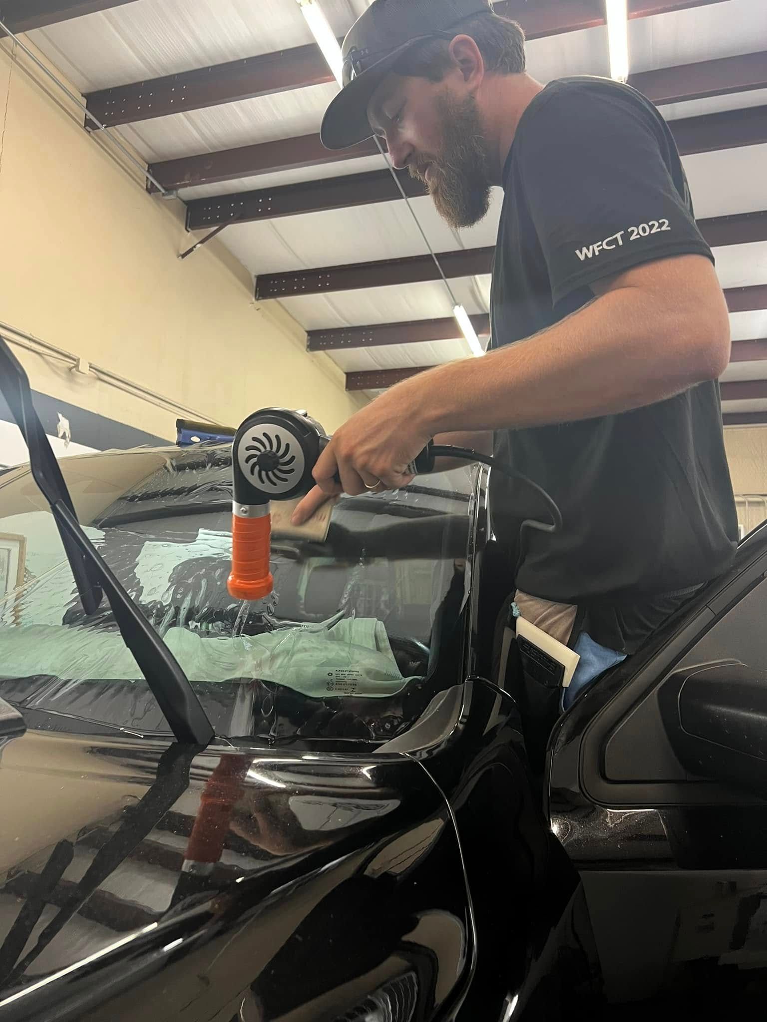 Technician polishing a black car windshield with a buffer in an auto shop